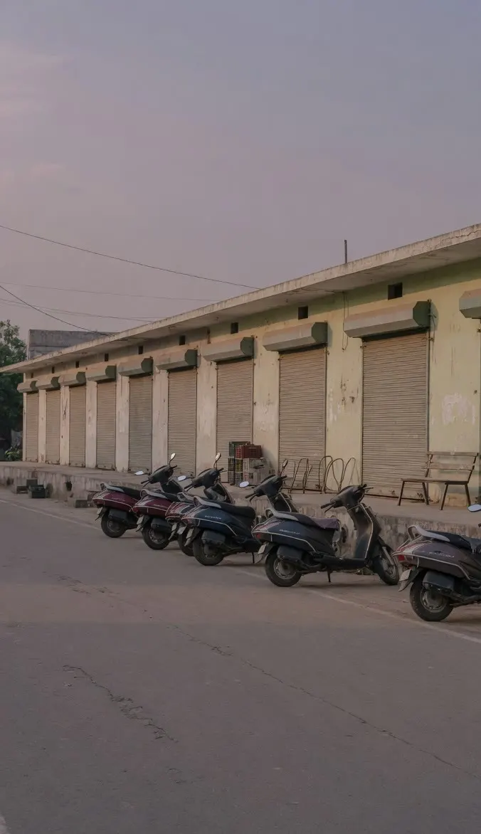 A dusk row of shuttered single-storey shops with parked scooters.
